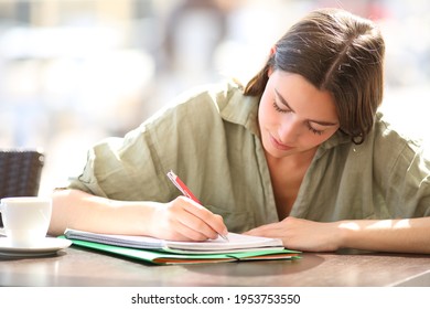 Concentrated student studying taking notes in a notebook in a coffee shop
