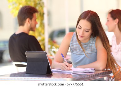 Concentrated Student Studying And Taking Notes In A Notebook Sitting In A Bar Terrace