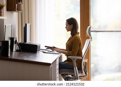 Concentrated successful young Caucasian businesswoman working on online project on computer in modern home workplace, sitting in comfortable office armchair, communicating distantly or web surfing. - Powered by Shutterstock