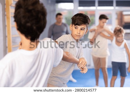 Concentrated teen boys practicing basic protection skills in training bout during self defense course in gym under guidance of instructor