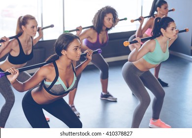 Concentrated at their workout. Beautiful young women with perfect bodies in sportswear exercising with barre while standing in front of window at gym