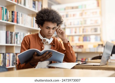 Concentrated thoughtful latin student guy, sitting at table in campus library, thinking about project or homework, looking at copybook - Powered by Shutterstock