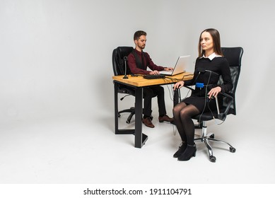 Concentrated, Thoughtful Woman Is In A Bright Room, Testing On A Computer Polygraph. Young Man Sitting At The Table And Looking At The Polygraph Screen And Polygraph Monitoring. The Concept Of Truth