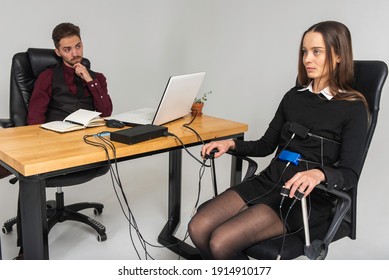 Concentrated, Thoughtful Woman Is In A Bright Room, Testing On A Computer Polygraph. Young Man Sitting At The Table And Looking At The Polygraph Screen And Polygraph Monitoring. The Concept Of Truth