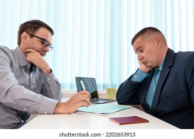 Concentrated Two Businessmen Sitting At Table, Involved In Serious Negotiations Or Contract Discussion In Blue Office. Focused Young Male Ceo Executive Manager Communicating With Partner Or Client.