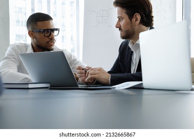 Concentrated two multiracial businessmen discussing online project presentation on computer, sitting together at table. Skilled diverse young colleagues brainstorming ideas in modern office. - Shutterstock ID 2132665867