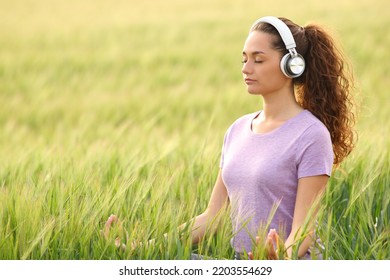 Concentrated woman wearing headphones doing yoga meditation with online tutorial in a field - Powered by Shutterstock