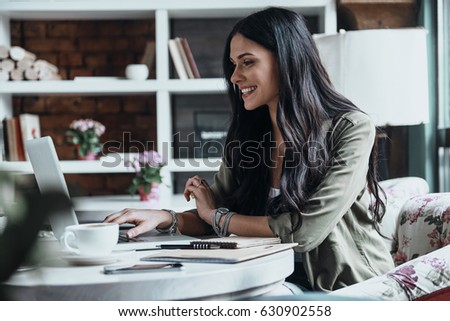 Concentrated at work. Beautiful young woman using laptop and looking at it while sitting at her working place