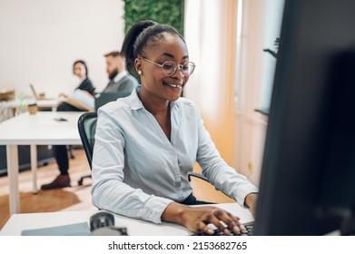 Concentrated Young African American Business Woman Working On A Laptop While Sitting At The Table In The Office. Confident Business Expert. E-commerce, Internet Technology Or Small Business Concept.