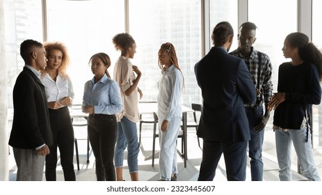 Concentrated young african american diverse business people employees colleagues talking chatting in small groups, discussing working issues or enjoying team building activity communication in office. - Powered by Shutterstock