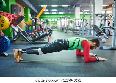 Concentrated young bearded man with prosthetic leg performing plank exercise in modern equipped with exercise machines - Powered by Shutterstock