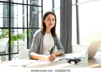 Concentrated young beautiful businesswoman working on laptop in bright modern office. - Shutterstock ID 2228820743