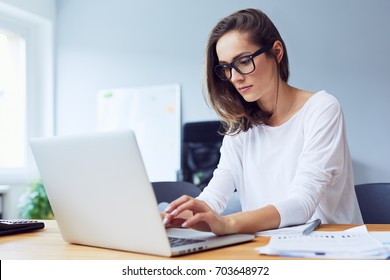 Concentrated young beautiful businesswoman working on laptop in bright modern office