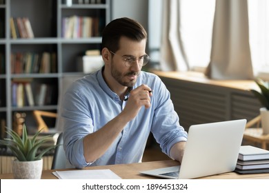 Jovem empresário concentrado em óculos olhando para a tela do laptop, informações de navegação na web na internet ou trabalhando remotamente on-line em home office, comunicação remota com o cliente ou estudo.