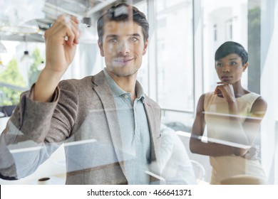 Concentrated young businessman working with african businesswoman and writing on transparent board in office - Powered by Shutterstock