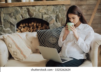 Concentrated Young Businesswoman In Official Clothes Sit On Sofa And Work Remote. Drink Hot Tea Or Coffee From Cup. Look At Laptop Screen. Have A Small Break