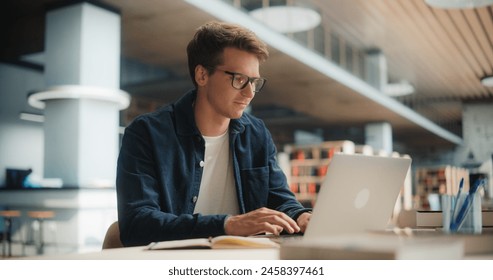 Concentrated Young Caucasian Male Student Working on His Laptop in a Modern Library. Man Engaged in Academic Research With Books Around, Focused on Screen. - Powered by Shutterstock