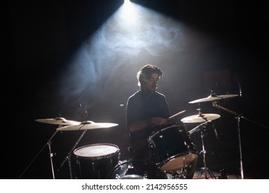 Concentrated young drummer training in dark hall with smoke in background. Rock musician rehearsing on drum set in studio. Drummer training concept - Powered by Shutterstock