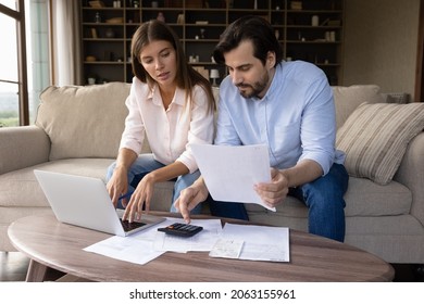 Concentrated Young Family Couple Calculating Expenditures, Analyzing Paper Bank Bills, Managing Monthly Budget, Planning Investment, Paying For Service Or Utilities Online Using Computer App.