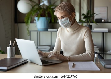 Concentrated Young Female Employee Worker Wearing Medical Facial Mask And Protective Gloves, Using Laptop In Office Or Working Remotely Online From Home, Healthcare Preventing Spreading Virus Habit.