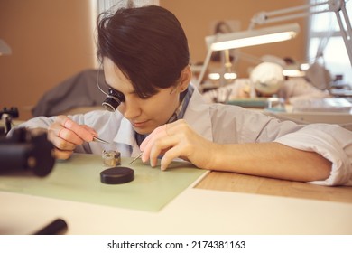 Concentrated young female watchmaker in lab coat sitting at table and using magnifying glass while assembling watch movements - Powered by Shutterstock