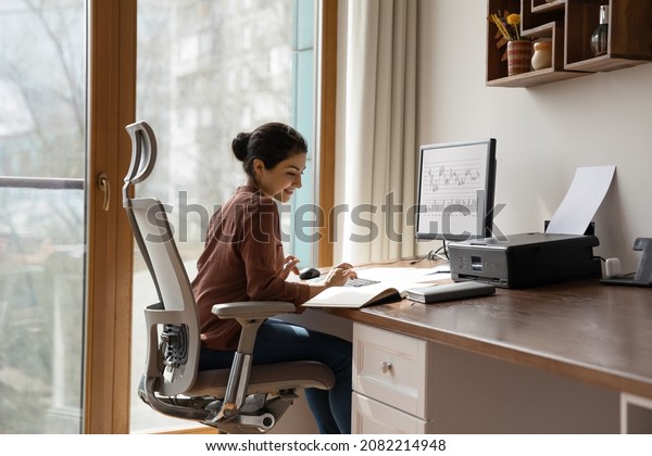 Concentrated young indian ethnicity woman\
sitting in comfortable adjustable ergonomic armchair with lumbar\
support, studying or working on computer in modern home office.\
distant workday\
concept.