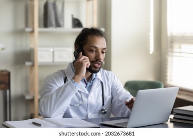 Concentrated Young Male African American General Practitioner Doctor Holding Distant Phone Call Conversation Working On Computer In Clinic Office, Giving Distant Professional Healthcare Consultation.