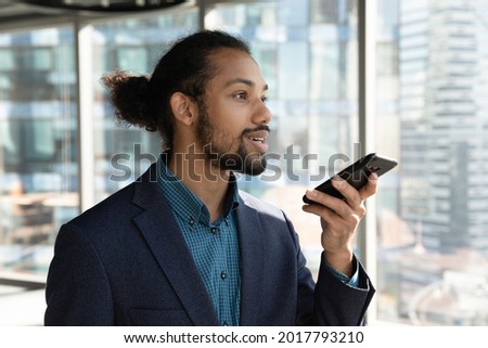 Concentrated young male african american multiracial ceo executive manager entrepreneur recording audio message on smartphone, dictating business ideas, setting reminder or using voice assistant.