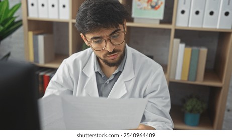 Concentrated young man with a beard in lab coat reading a document in a clinic interior. - Powered by Shutterstock