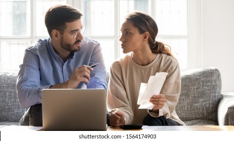 Concentrated Young Man In Eyeglasses Sitting On Couch With Mixed Race Woman, Managing Family Monthly Budget Together. Focused Married Couple Using Computer Banking Application, Counting Bills.