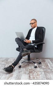 Concentrated Young Man In Glasses Sitting In Office Chair And Using Laptop