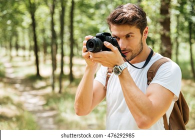 Concentrated young man photographer taking pictures with modern photo camera in forest Stock Photo