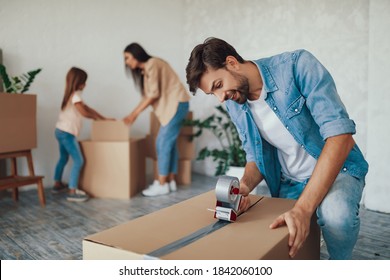 Concentrated young man putting tape on a cardboard box while whole family preparing to move out of the house