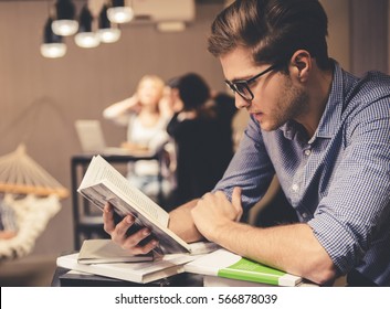 Concentrated Young Man Is Reading A Book While Working Hard In The Modern Library