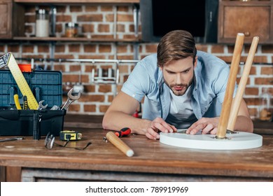 concentrated young man repairing stool with tools at home