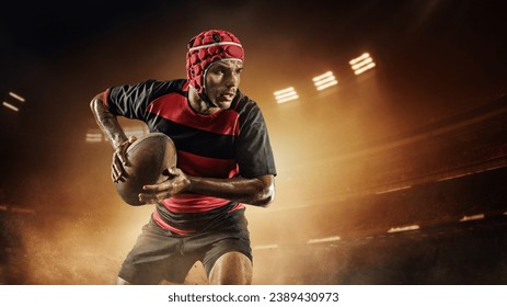 Concentrated young man, rugby player in uniform with ball standing on dark empty field with flashlights and mist. Concept of professional sport, competition, motivation, game, championship - Powered by Shutterstock