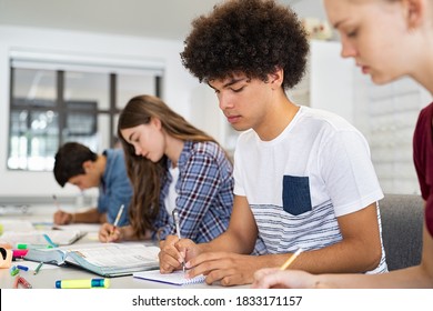 Concentrated young man studying in classroom with friends sitting in a row. College student concentrating on studies while taking notes. African american high school guy preparing exam with classmates - Powered by Shutterstock