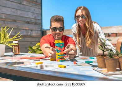 Concentrated young man with sunglasses pushing wooden stacking piece game piece next to his female friend in rooftop on a summer party. Selective focus on jenga tower game. - Powered by Shutterstock