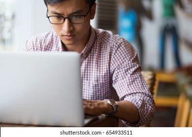 Concentrated Young Man Typing On Laptop In Cafe