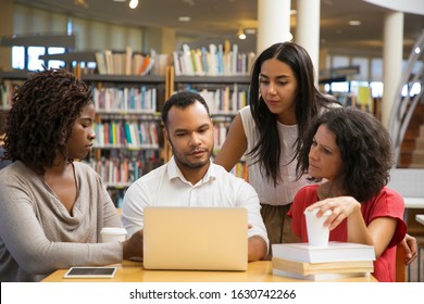 Concentrated young people reading information from laptop. Cheerful students working with laptop at library. Education concept - Powered by Shutterstock
