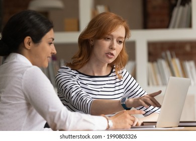 Concentrated young red-haired business lady discussing online project or analyzing sales data statistics with indian colleague in office. Focused young mixed race employees working on computer. - Powered by Shutterstock