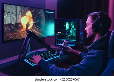Concentrated young streamer man winning space shooter online competition talking at professional microphone in gaming room studio. Pro gamer playing online video games and streaming during tournament - Shutterstock ID 2150257067