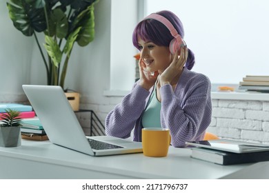 Concentrated Young Woman With Purple Hair Using Laptop While Sitting At Her Working Place