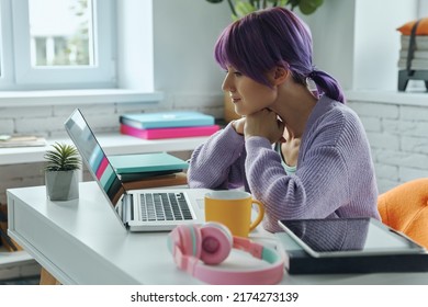 Concentrated Young Woman With Purple Hair Working On Laptop While Sitting At Her Working Place