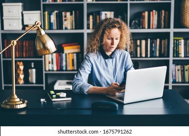 Concentrated Young Woman Sitting At Desk In Library And Working On Laptop And Phone From Home.