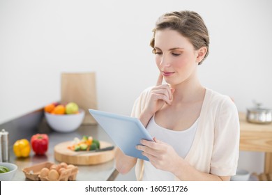 Concentrating young woman using her tablet standing in her kitchen at home