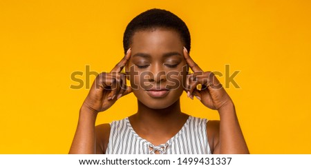 Concentration. Afro girl holding fingers on temples, thinking hard, trying to concentrate, yellow studio background