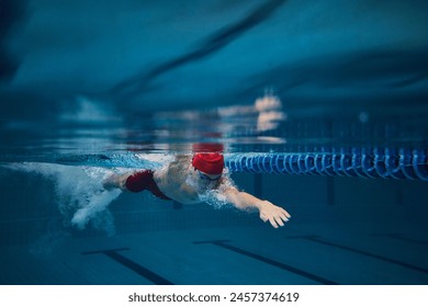 Concentration. Competitive young man, swimming athlete in goggles and red cap in motion, training in pool indoors. Concept of professional sport, health, endurance, strength, active lifestyle - Powered by Shutterstock