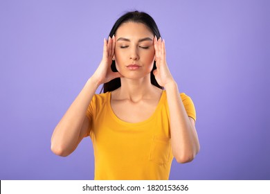 Concentration Concept. Portrait of young woman holding fingers on temples, thinking hard, trying to concentrate, isolated over purple studio background. Lady doing breathing yoga practice