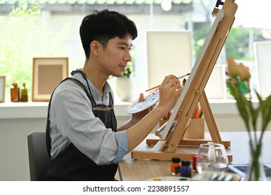 Concentred man painting picture on canvas with oil paints in bright art studio. Leisure activity and art concept - Shutterstock ID 2238891557